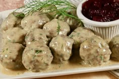 meatballs covered in gravy next to a small bowl of cranberry sauce