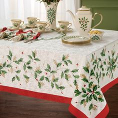 a christmas table cloth with holly designs and red roses in a vase on the table