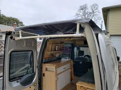 a van with the door open is parked in front of a house and has an awning on it's roof