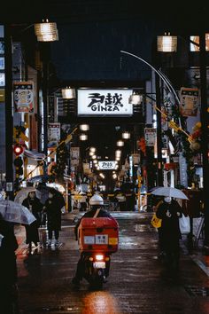 a person riding a motorcycle on a city street at night with an umbrella over their head