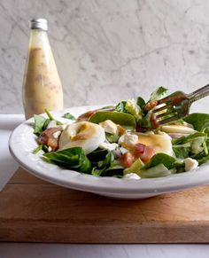 a white plate topped with salad next to a bottle of dressing