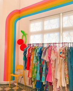 a room filled with lots of colorful clothing hanging on clothes racks next to a window