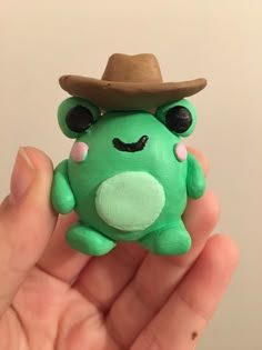 a hand holding a small green frog with a hat on it's head and eyes