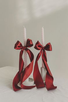 two candles are wrapped in red ribbon and placed on a white surface with a candle holder