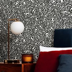 a bedroom with black and white wallpaper, red pillows and a lamp on the nightstand