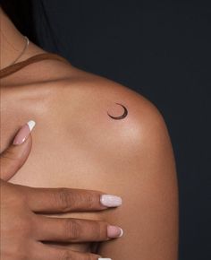 a woman's shoulder with a small crescent tattoo on the left side of her arm