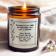 a candle with a poem on it sitting next to some dried flowers and a white cloth