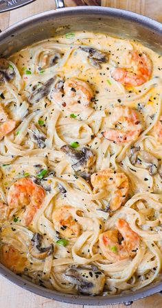 pasta with shrimp and mushrooms in a skillet on a wooden counter top, ready to be eaten