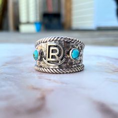 This handsome Gentlemen Cattle Brand Ring, made with sterling silver, adds the perfect touch of western style to any ensemble. The detailed craftsmanship of this classic ring showcases the brand with our design and artisan flare. A must-have for any modern-day cowboy. Features: 13mm wide in front 4mm wide on back Solid sterling silver .925 2 Kingman turquoise stone optional Customizable with brand or initial Hammered texture with rope border Handmade in PA Made to order allow 2 to 4 weeks for pr Urban Cowgirl, Cattle Brands, Rope Border, Bracelet Size Chart, Kingman Turquoise, Grad Gifts, Classic Ring, Leather Jewelry, Turquoise Stone