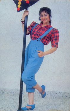 a woman in overalls is leaning on a pole holding a flag and posing for the camera