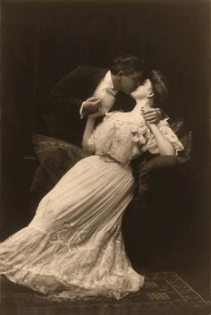 an old black and white photo of a woman in a long dress kissing a man