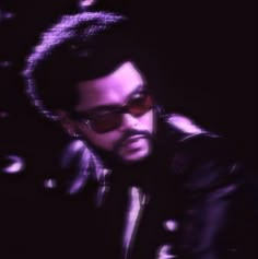 a man wearing sunglasses and a leather jacket is looking at his cell phone in the dark