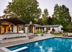 an outdoor swimming pool in front of a house with patio furniture and landscaping around it