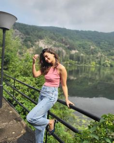 a woman standing on top of a metal rail next to a body of water with trees in the background