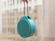 a hand holding a blue speaker in front of a window