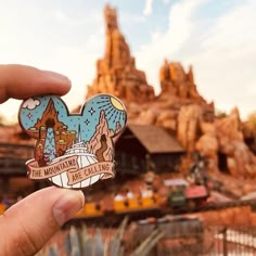 someone holding up a disneyland pin with the theme park in the backgroung