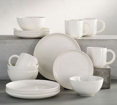 white dishes and cups are stacked on top of each other in front of a gray wall