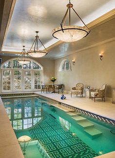 an indoor swimming pool with chairs and tables in the corner, next to it is a chandelier