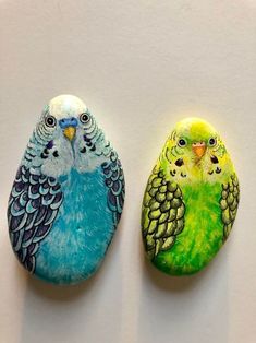 two painted birds sitting next to each other on top of a white surface with green and blue feathers