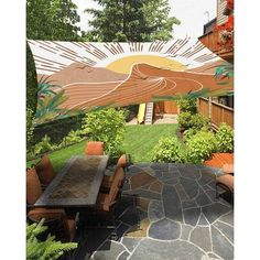 an outdoor dining area with stone patio and large painting on the wall above it's table