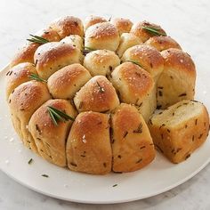 a white plate topped with bread rolls covered in rosemary sprinkles on top of a marble counter