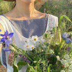 a woman wearing a straw hat holding a bouquet of wildflowers and daisies