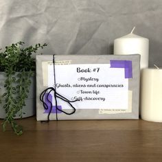 a book sitting on top of a wooden table next to a candle and some plants