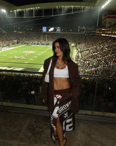 a woman standing in front of a crowd at a football game wearing a skirt and jacket