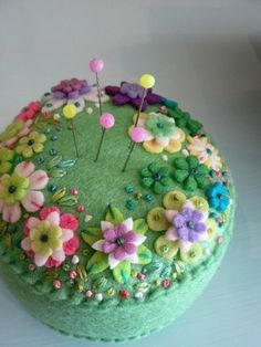 a green round box with flowers and pins on the top, sitting on a table