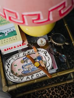 a table topped with books and glasses on top of a metal tray next to a yellow vase