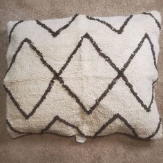 a white and black pillow sitting on top of a carpeted floor next to a wall