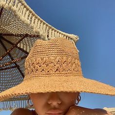 a woman wearing a large straw hat on top of her head and under an umbrella