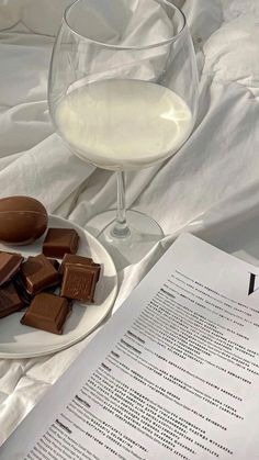 a glass of wine and some chocolates on a plate next to an open book