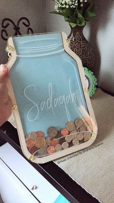 a person holding a glass jar with coins in it and the word sadagon written on it