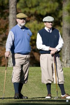 two older men standing next to each other on top of a grass covered golf field