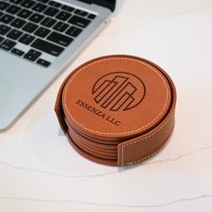 a stack of brown leather coasters sitting next to a laptop on a white table