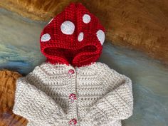 a red and white knitted jacket with polka dots on the hood is sitting on a piece of wood