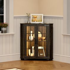 a cabinet with glass doors is in the middle of a room that has wood floors and white walls