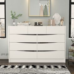 a white dresser sitting in front of a mirror on top of a wooden floor next to a rug