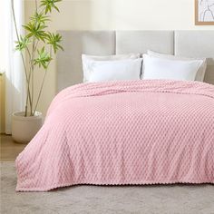 a bed with a pink comforter and pillows in a room next to a potted plant