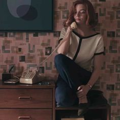 a woman sitting on top of a desk talking on a phone