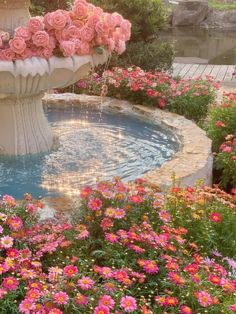 a fountain with pink flowers in it surrounded by greenery