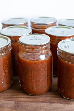 several jars of tomato sauce sit on a wooden table with labels in the top and bottom