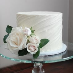 a close up of a cake on a glass platter with white frosting and flowers