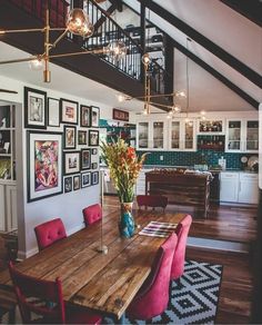 a dining room table with red chairs and pictures on the wall behind it in front of a stair case