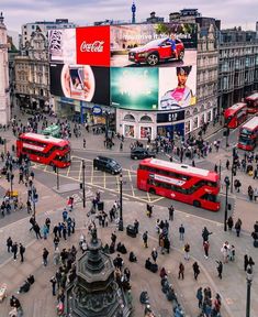 a busy city intersection with double decker buses and people walking on the sidewalk in front of it