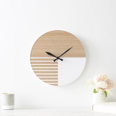 a clock that is on the wall next to a white vase with flowers in it