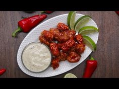 a white plate topped with chicken wings next to a small bowl of ranch dressing and sliced green peppers