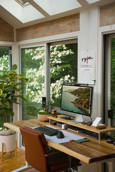 a desk with a computer monitor and keyboard on top of it next to a potted plant