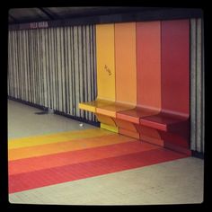 a bench sitting in front of a wall with colorful stripes on it's sides